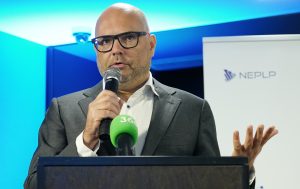 NEPLP pārstāvis uzstājas publiskā pasākumā ar mikrofonu.