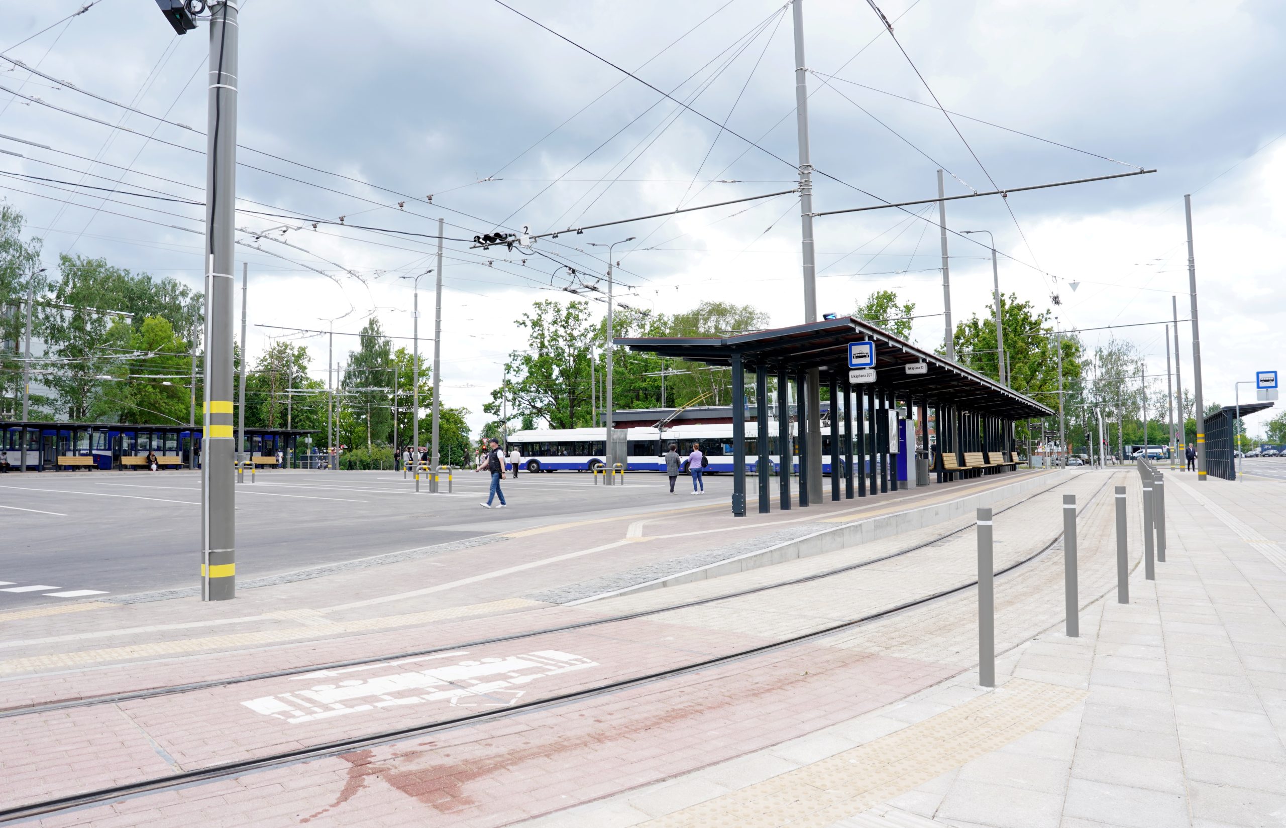 Sabiedriskā transporta pieturvieta ar tramvaja sliedēm un autobusiem pilsētvidē.