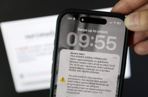 Mobilā tālruņa ekrānā redzams šūnapraides brīdinājuma paziņojums par trauksmes sirēnu pārbaudi Latvijā.