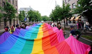 Riga Pride gājiena dalībnieki Rīgas centrā nes lielu varavīksnes karogu.