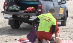 Pludmales glābējs demonstrē atdzīvināšanas pasākumus uz manekena pludmalē pie glābšanas dienesta automašīnas.