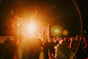 Valmiermuižas etnomūzikas festivāla vakara koncerts ar izgaismotu skatuvi un apmeklētājiem parkā.
