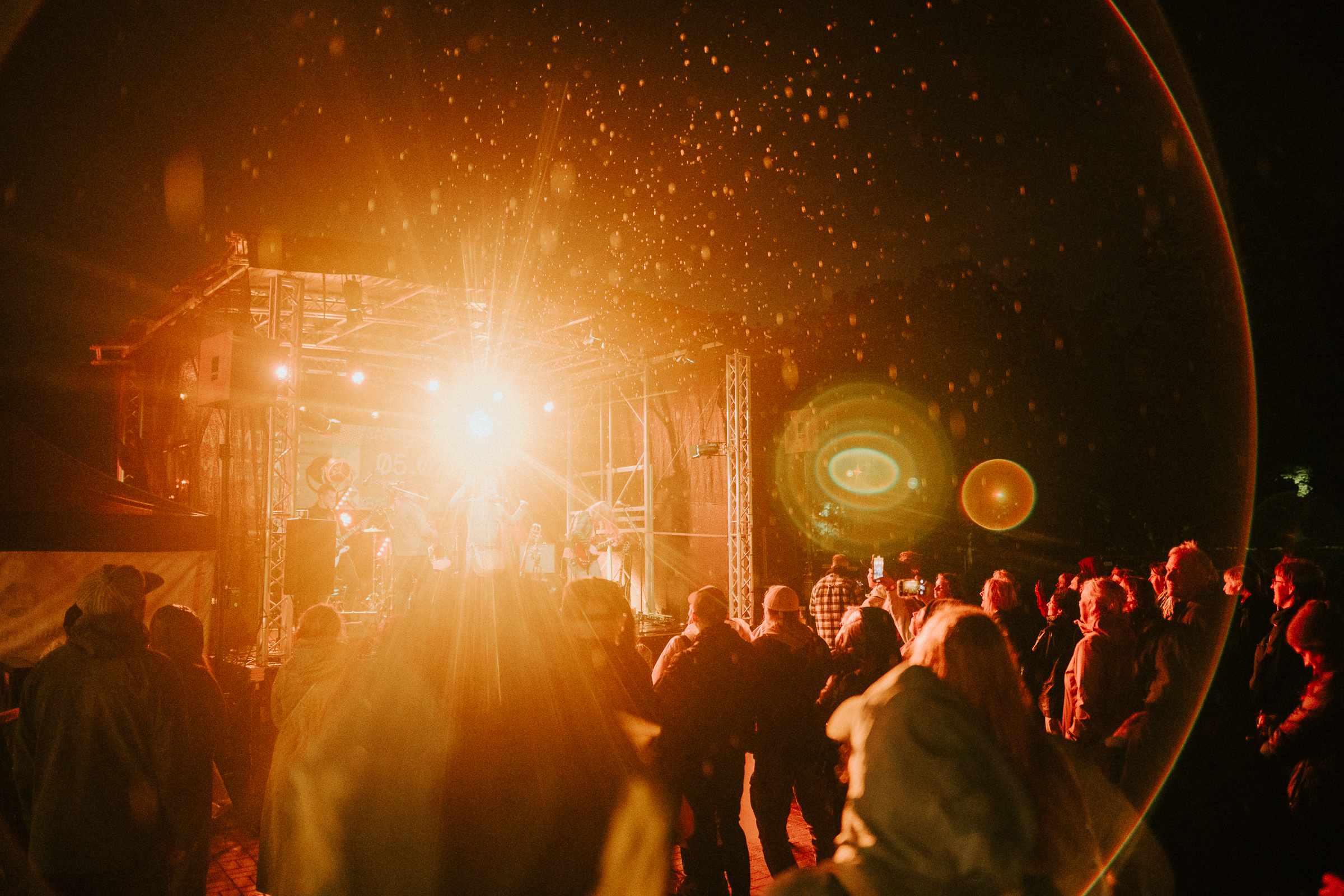 Valmiermuižas etnomūzikas festivāla vakara koncerts ar izgaismotu skatuvi un apmeklētājiem parkā.