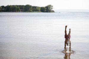 Bērns jūras seklumā stāv uz rokām, ūdenim šļakstot apkārt saulainā vasaras dienā.
