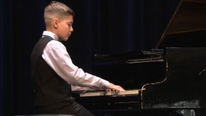 Jauns pianists uzstājas koncertā, spēlējot flīģeli uz skatuves.