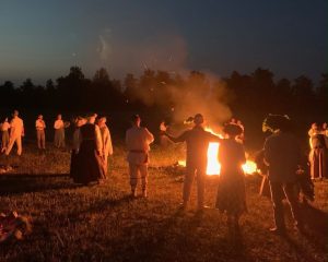 Cilvēki tradicionālos tērpos pulcējušies ap Jāņu ugunskuru vasaras saulgriežu svinībās.