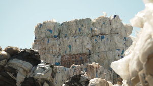 Saplēvēti plastmasas atkritumu maisu ķīpu krāvumi atkritumu pārstrādes laukumā.