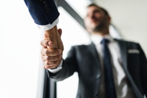 Divi biznesa pārstāvji sarokojas biroja vidē, simbolizējot sadarbību vai vienošanos.