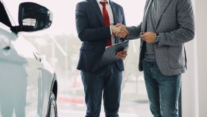 Autosalona darbinieks un klients paspiež rokas pie automašīnas pēc līguma noslēgšanas.