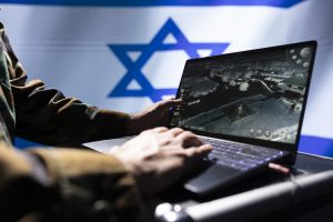 Persona pie klēpjdatora analizē militārus datus uz Izraēlas karoga fona.