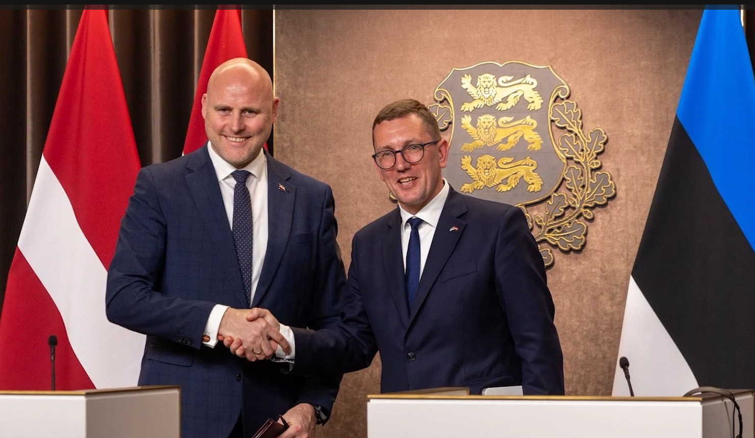 Latvijas un Igaunijas amatpersonas sarokojas pēc tikšanās, fonā abu valstu karogi.