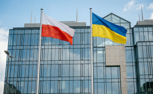 Polijas un Ukrainas karogi plīvo pie modernas stikla ēkas.