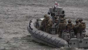 Militārpersonas pilnā ekipējumā pārvietojas ar ātrgaitas piepūšamo laivu jūrā militāro mācību laikā.