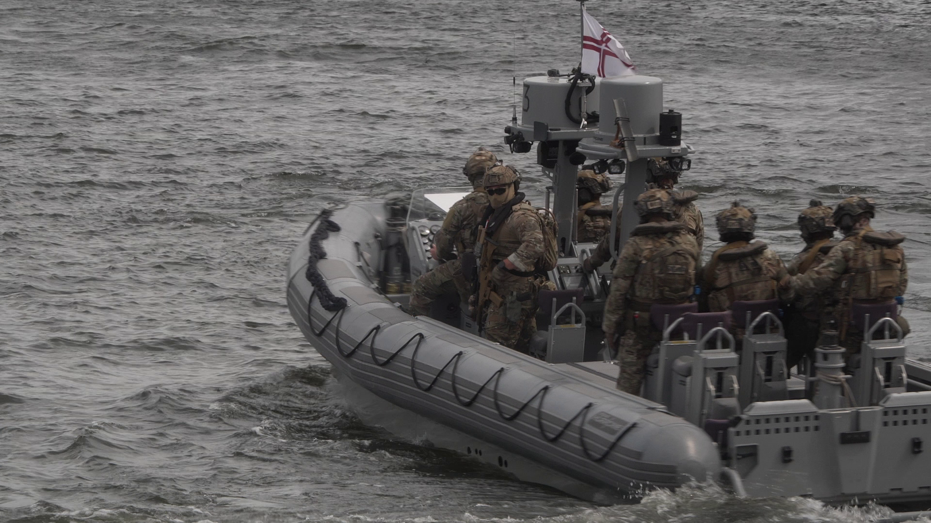 Militārpersonas pilnā ekipējumā pārvietojas ar ātrgaitas piepūšamo laivu jūrā militāro mācību laikā.
