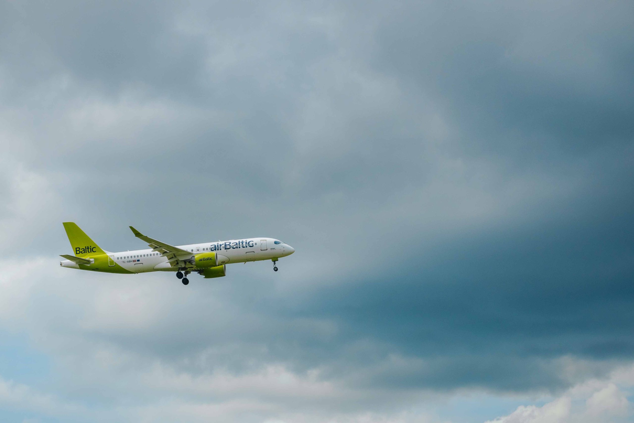 airBaltic pasažieru lidmašīna lido mākoņainās debesīs pirms nosēšanās.