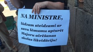 Protestētāja tur plakātu ar aicinājumu apturēt Majoru airēšanas skolas likvidāciju.