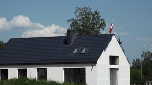 Jaunuzcelta privātmāja ar tumšu jumtu un Latvijas karogu pie ēkas.