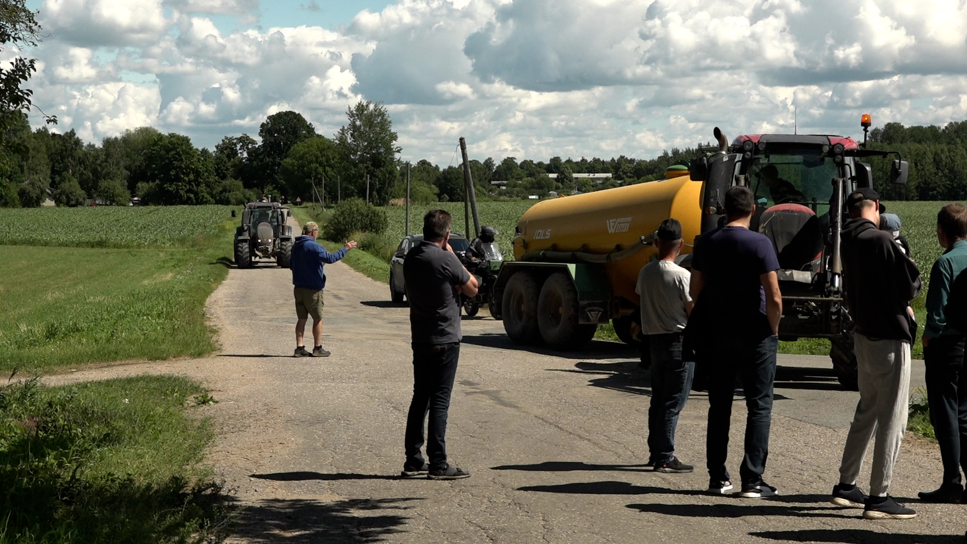 Vietējie iedzīvotāji un lauksaimnieki pie traktortehnikas uz lauku ceļa Lēdurgas apkārtnē.