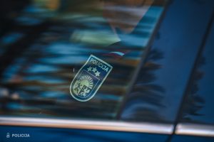 Valsts policijas darbinieka formas uzšuve ar Latvijas karogu uz dienesta automašīnas fona.