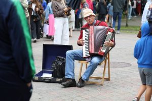 Ielu muzikants spēlē akordeonu Jūras svētku laikā, kamēr garām dodas pasākuma apmeklētāji.