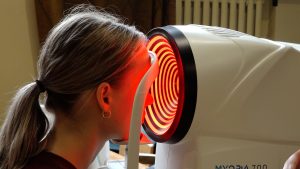 Pētījuma dalībniece veic acu mērījumus ar specializētu diagnostikas iekārtu.