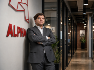 “Alpha Baltic Media” pārstāvis uzņēmuma birojā pie “Alpha” logotipa