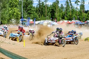 Blakusvāģu motokrosa ekipāžas sacenšas Madonas trasē, gaisā paceļot putekļu mākoņus.