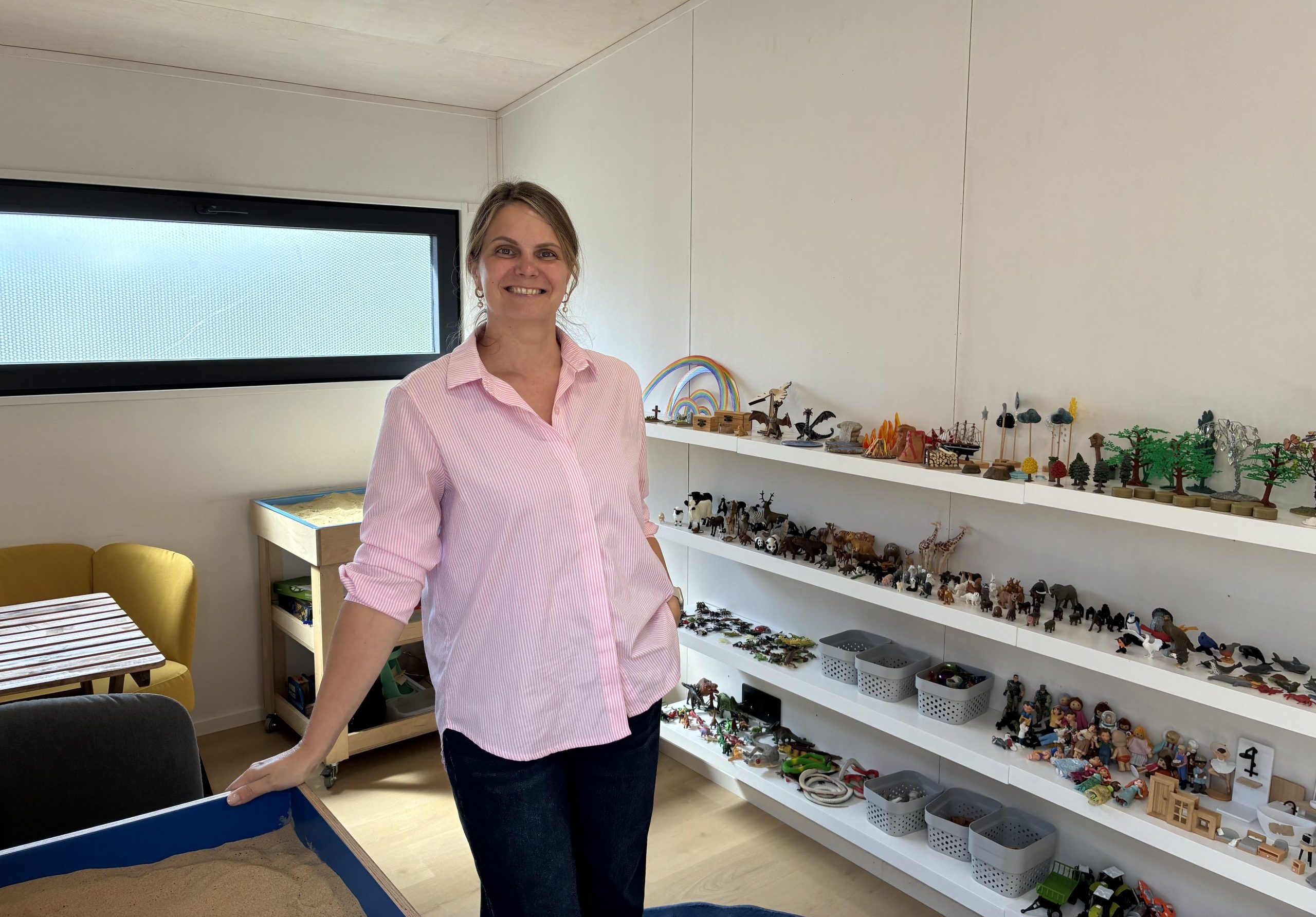 Terapeite Ilze Žilde mobilajā smilšu terapijas kabinetā līdzās terapijas materiāliem un smilšu galdam.
