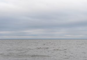 Pelēka jūra zem apmākušām debesīm.