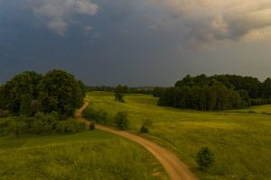 Negaisa mākoņi savelkas virs lauku ainavas ar grantētu ceļu.