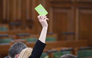 Saeimas sēdē deputāte paceļ zaļo balsošanas kartīti, balsojot par likumprojektu.