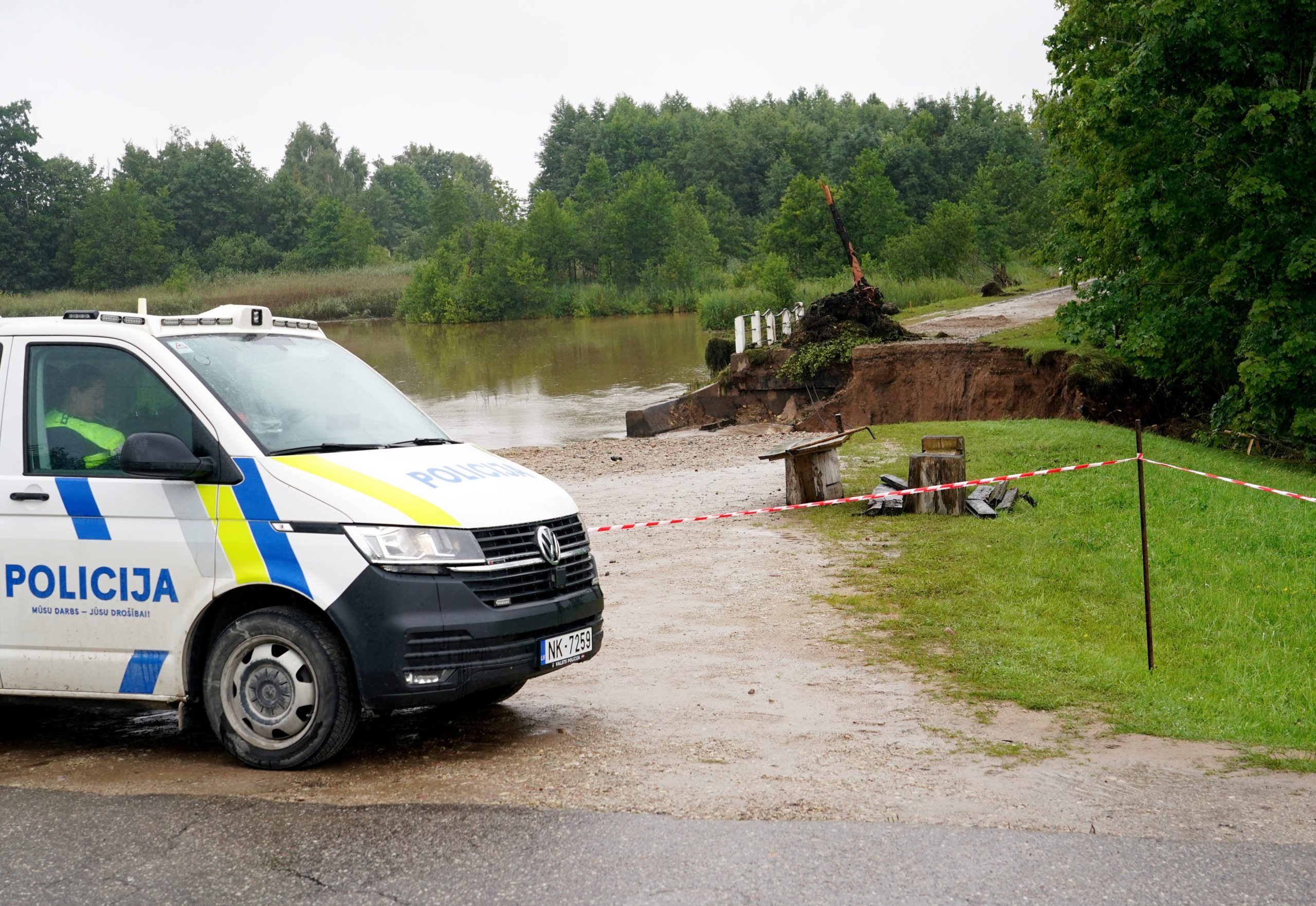 Policijas automašīna pie lietus izskalota ceļa un sabrukuša tilta.