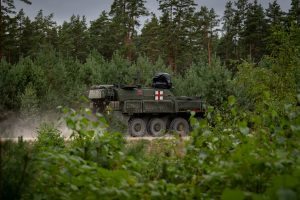 NATO militārās medicīnas transportlīdzeklis pārvietojas pa meža ceļu mācību laikā.