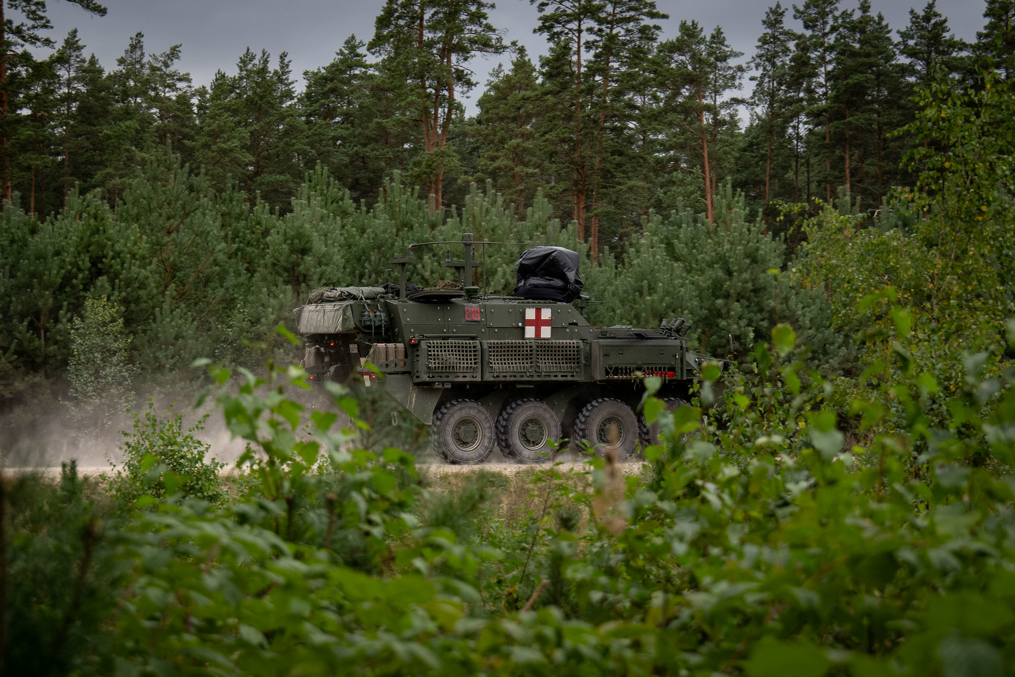 NATO militārās medicīnas transportlīdzeklis pārvietojas pa meža ceļu mācību laikā.