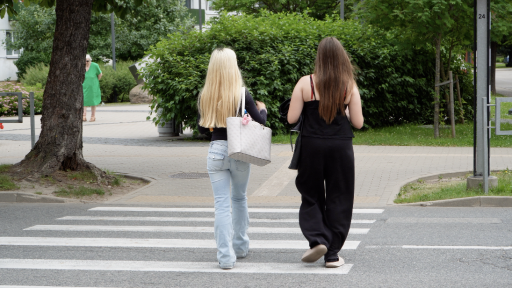 Divas jaunietes šķērso gājēju pāreju pilsētvidē, dodoties pāri ielai.