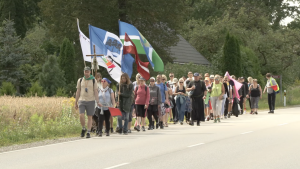 Svētceļnieku grupa ar karogiem dodas pa ceļu uz Aglonu, ejot organizētā gājienā.