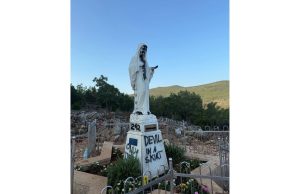 Vandaļu apķēpāta Jaunavas Marijas statuja Medžugorjē ar melnu krāsu un uzrakstiem uz pamatnes.
