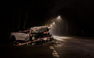 Smagi bojāta automašīna pēc frontālas sadursmes uz tumšas ielas nakts laikā.
