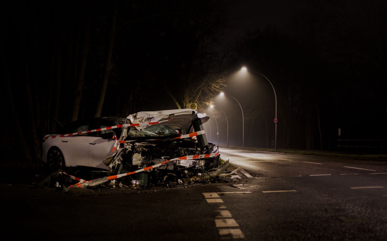 Smagi bojāta automašīna pēc frontālas sadursmes uz tumšas ielas nakts laikā.