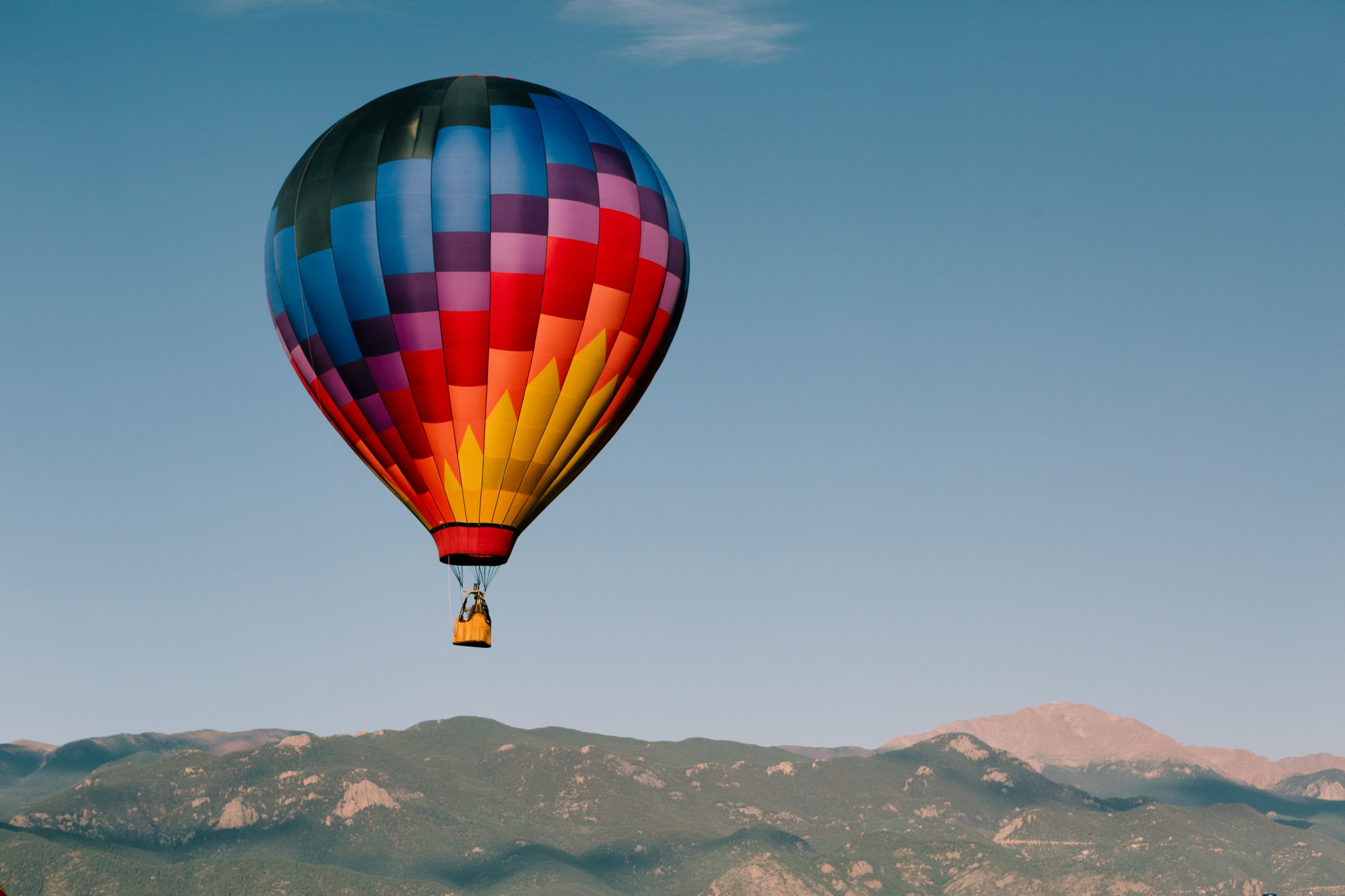 Krāsains gaisa balons lido virs kalnu ainavas vasaras dienā