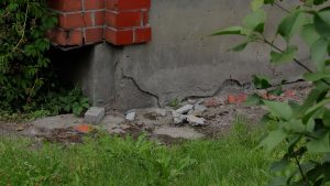 Plaisas daudzdzīvokļu mājas pamatos un bojāts cokols pirms atjaunošanas darbiem.