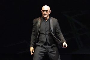 Amerikāņu reperis un dziedātājs Pitbull uzstājas uz skatuves ar mikrofonu rokā.