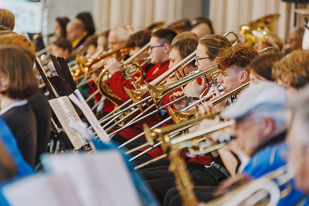 Pūtēju orķestra mūziķi spēlē trombonus un citus pūšaminstrumentus