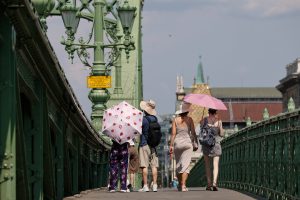 Cilvēki ar saulessargiem šķērso Brīvības tiltu Budapeštā Eiropas karstuma viļņa laikā