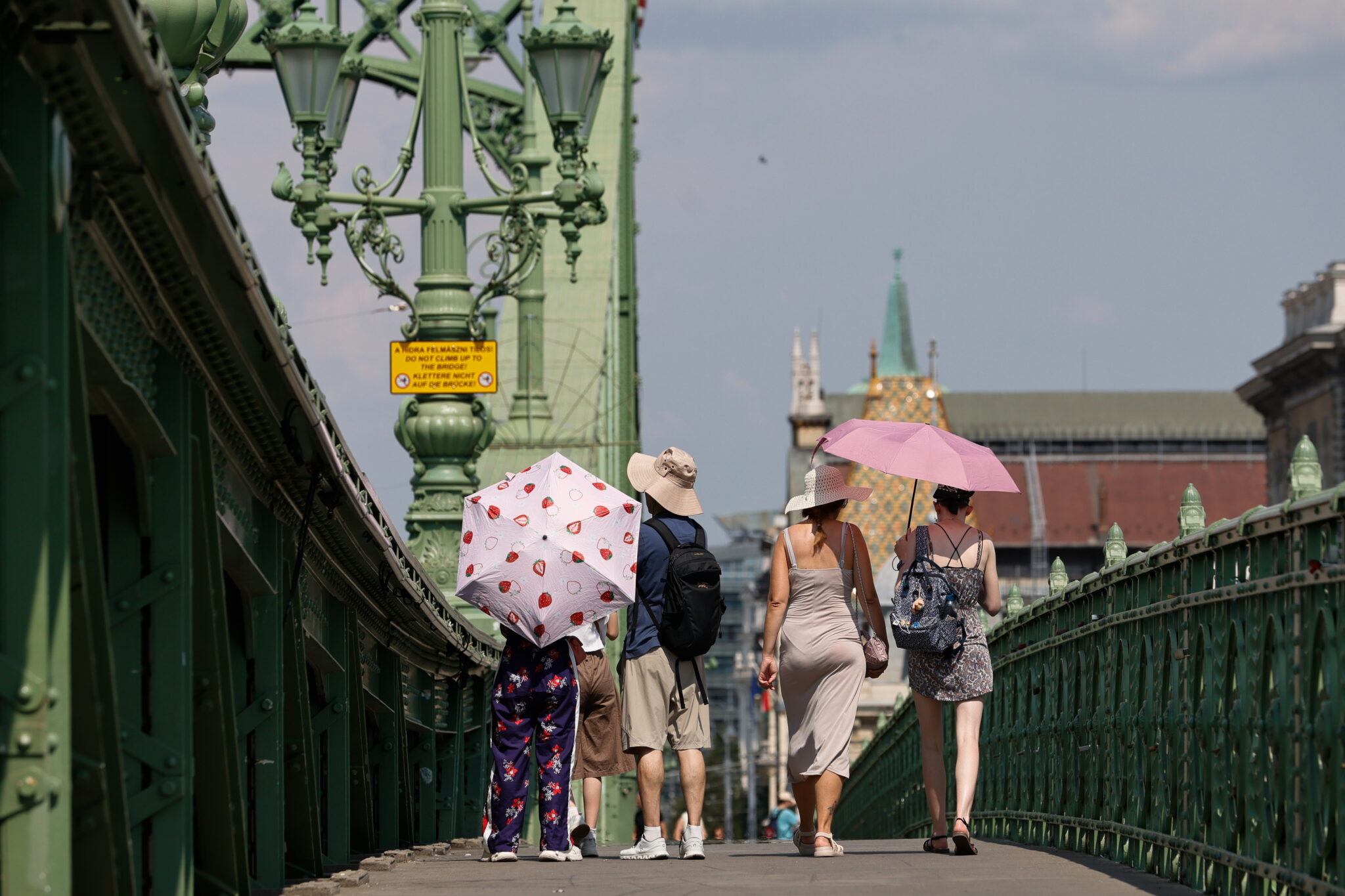 Cilvēki ar saulessargiem šķērso Brīvības tiltu Budapeštā Eiropas karstuma viļņa laikā