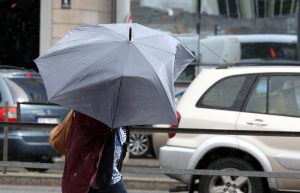 Cilvēks ar lietussargu stipra lietus laikā pilsētā