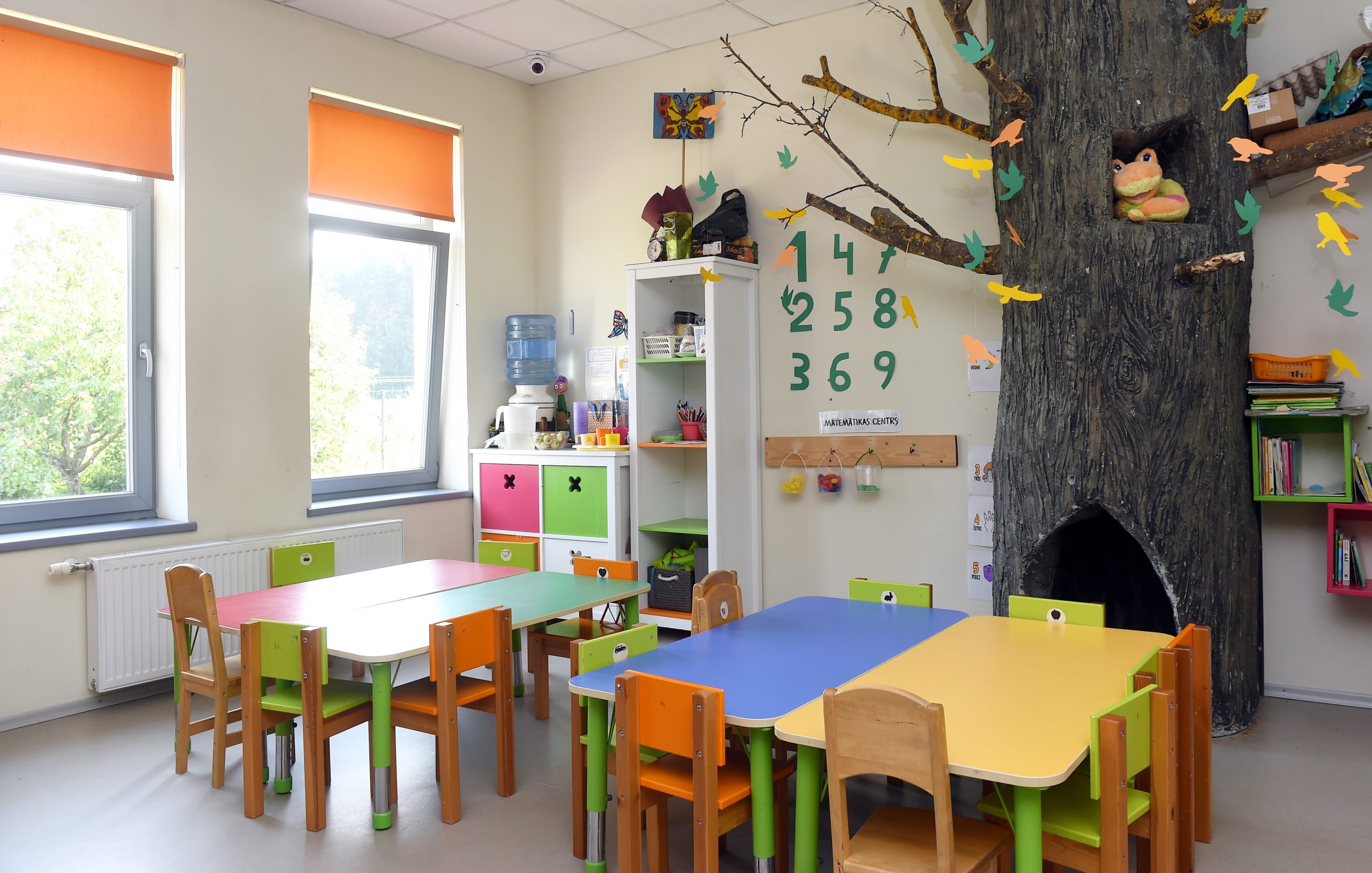 Pirmsskolas izglītības iestādes grupiņas telpa ar bērnu galdiem un krēsliem
