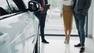 Pircēji autosalonā apskata automobili un konsultējas ar pārdevēju par iegādes nosacījumiem.