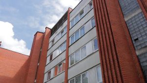 Daudzdzīvokļu dzīvojamās mājas fasāde ar vairākiem stāviem un logiem.