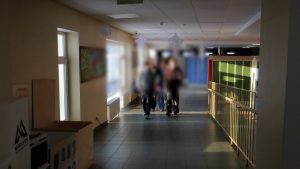 Cilvēki skolas gaitenī pie skolēnu skapīšiem